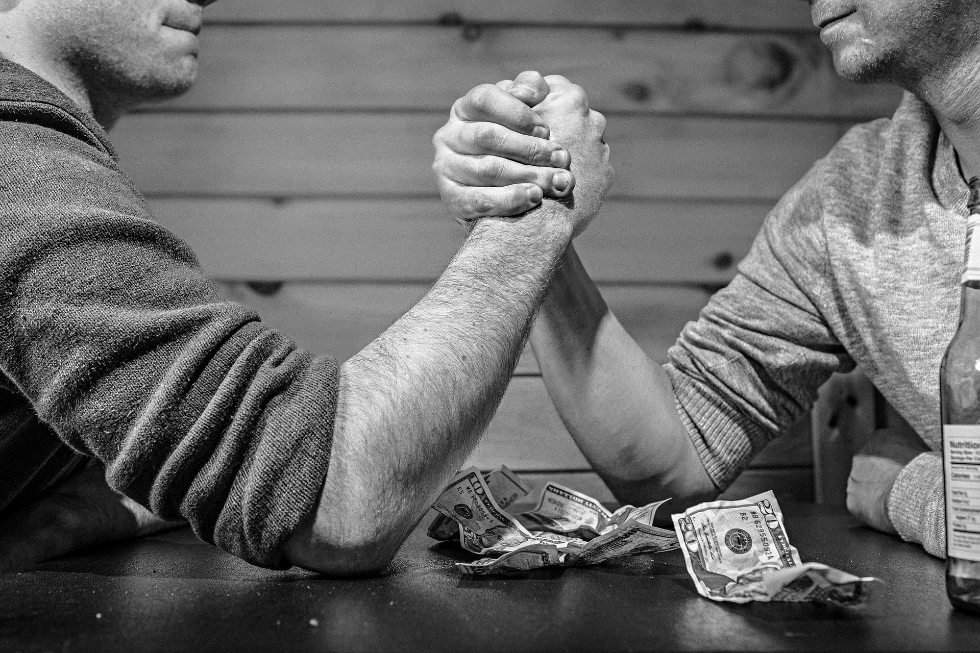 A close-up of two men arm wrestling over money, representing the ongoing debate around the question: is sports betting legal in Georgia?