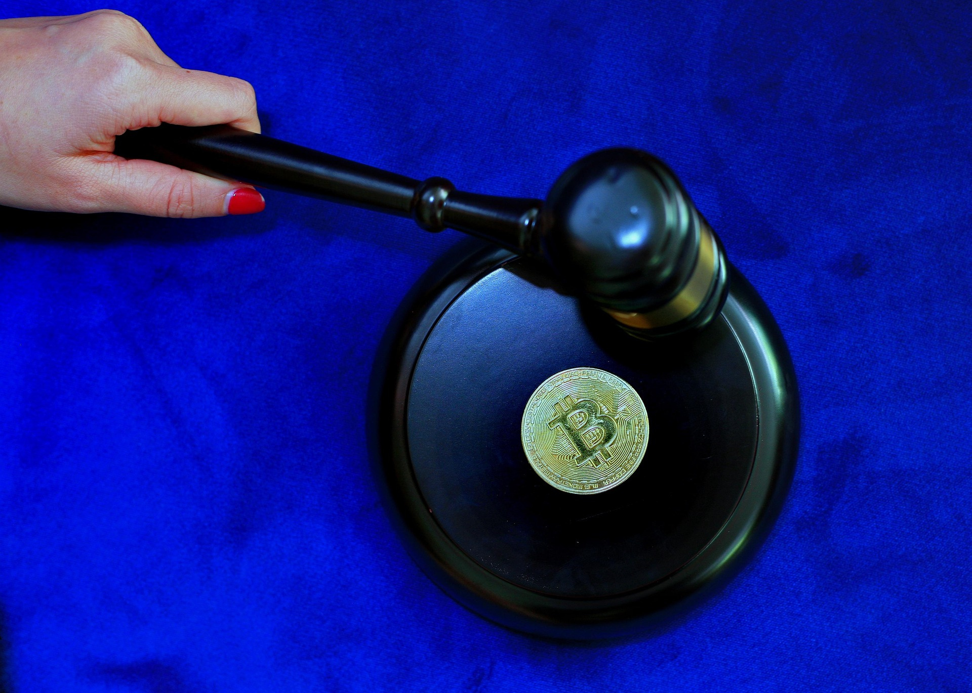A judge’s gavel strike about to the legal status of cryptocurrency, a golden Bitcoin coin, symbolizing cryptocurrency regulation or legal judgment on digital assets, with a blue background.