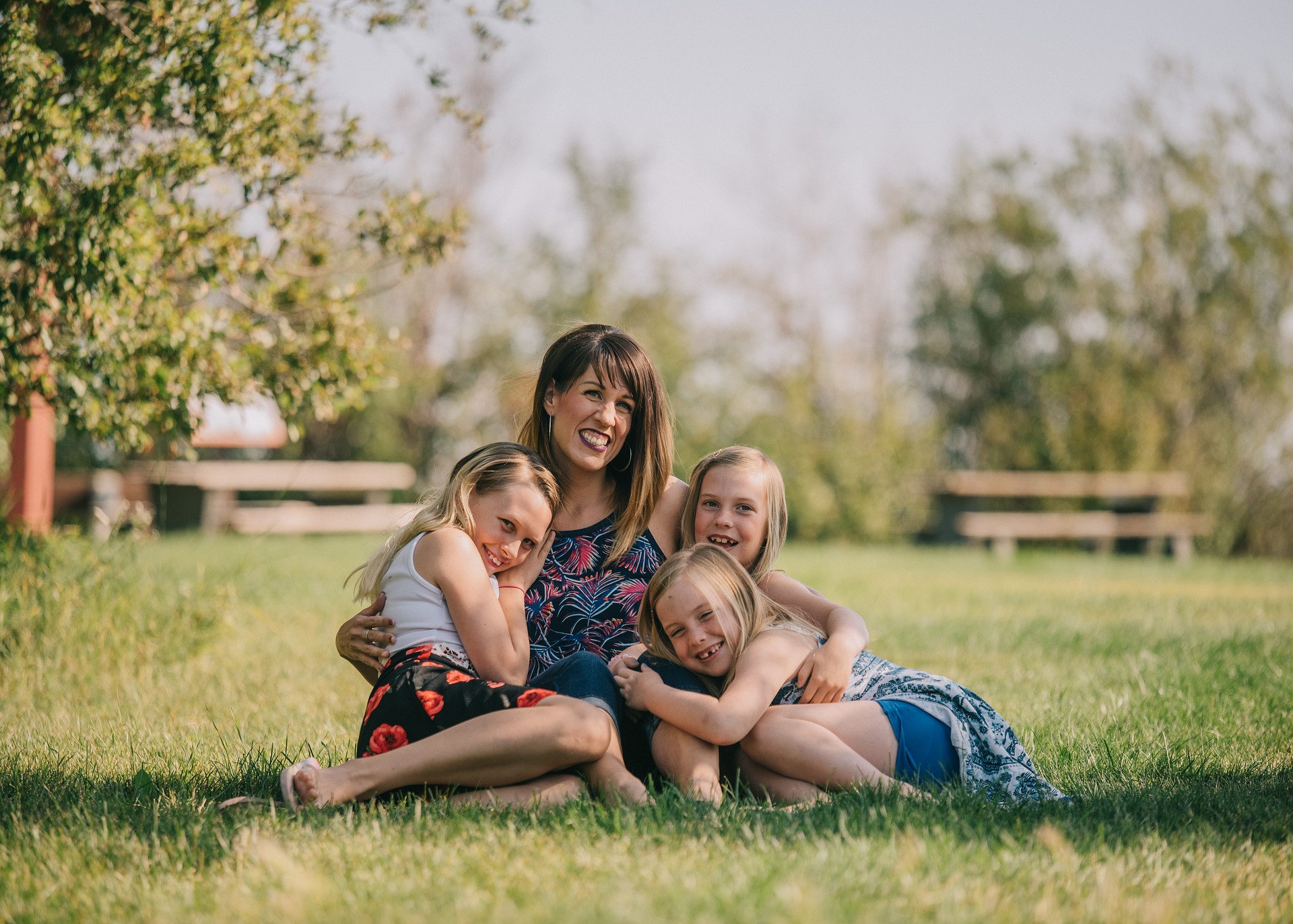 Mother sitting on the grass joyfully hugging her three daughters—symbolizing love, care, and the emotional strength behind seeking full custody of a child as a mother.